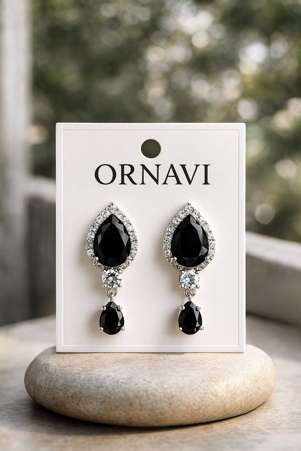 Black teardrop earrings on a white ORNAVI card with a blurred natural background