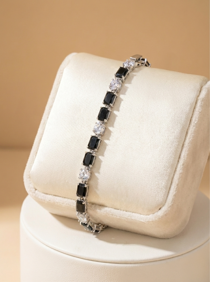 Bracelet with black and clear stones on a beige cushion against a beige background