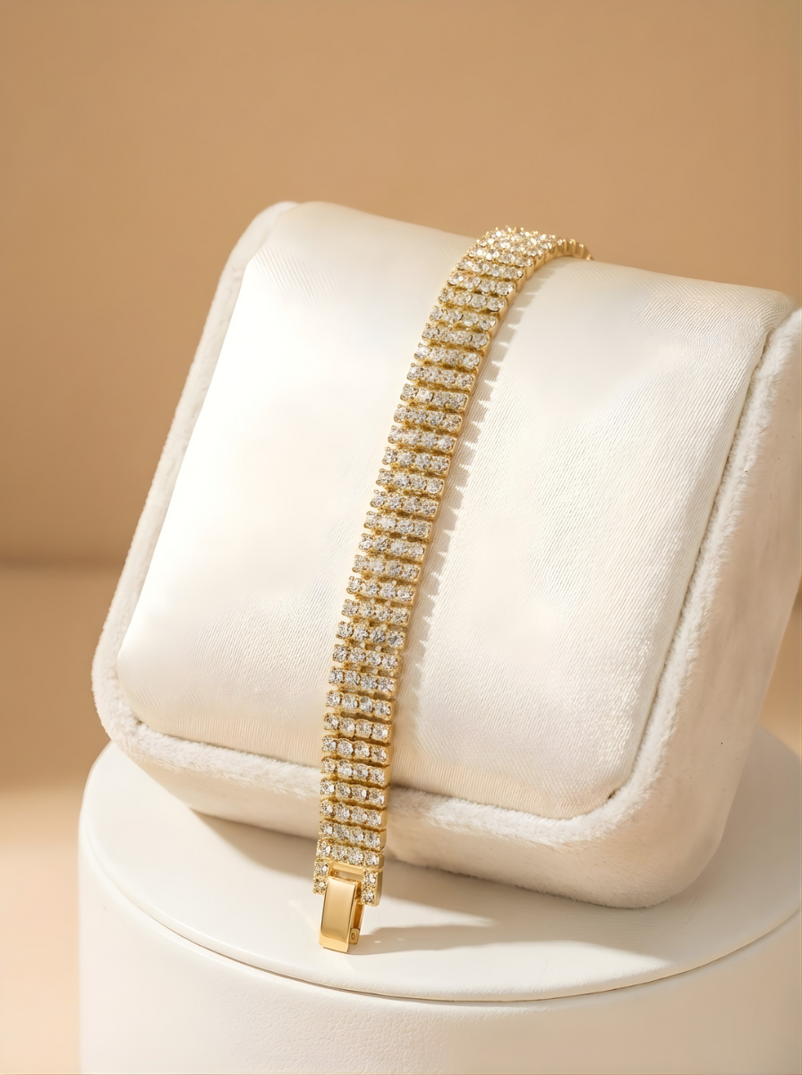 Gold bracelet with clear stones on a white cushion against a beige background