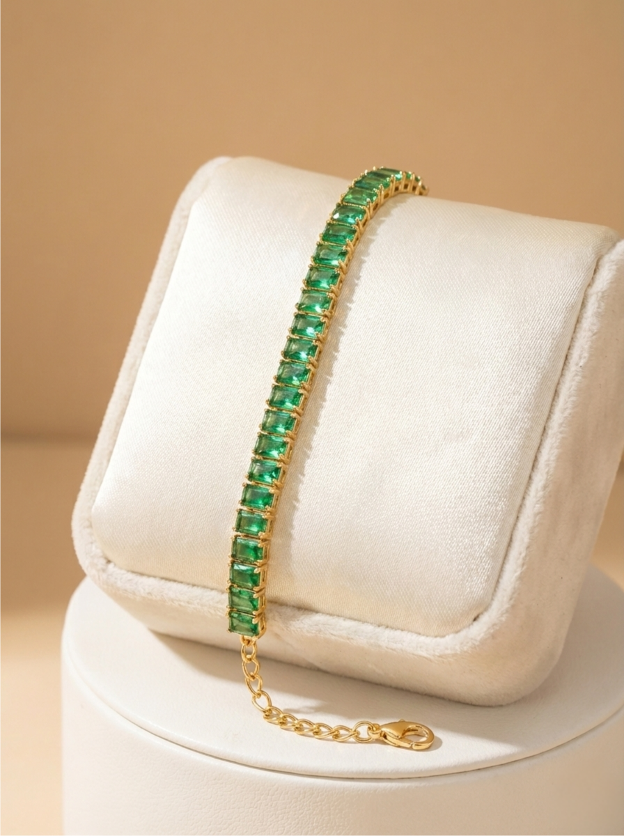 Green emerald bracelet on a gold chain on a white cushion with a beige background