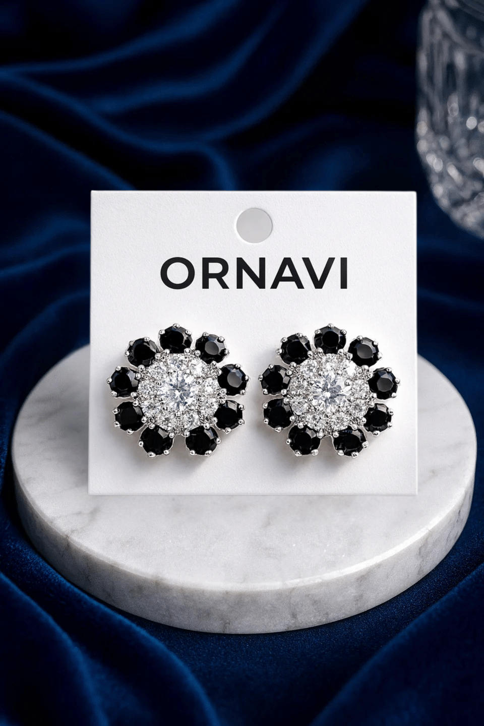 Heart-shaped earrings with black and clear stones on a white card labeled 'ORNAVI' against a dark blue fabric background.