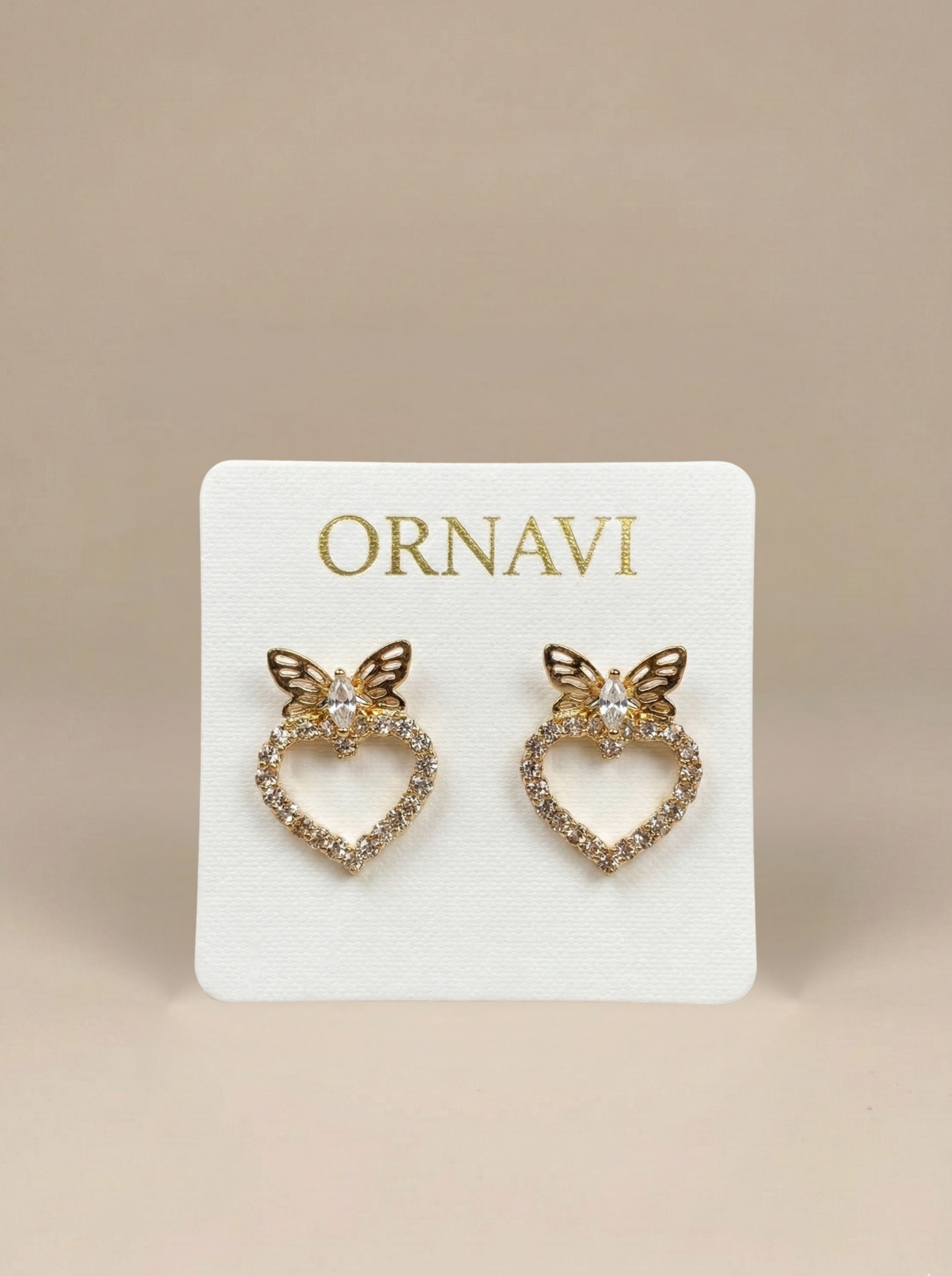 Heart-shaped earrings with butterfly details on a ORNAVI branded card against a beige background