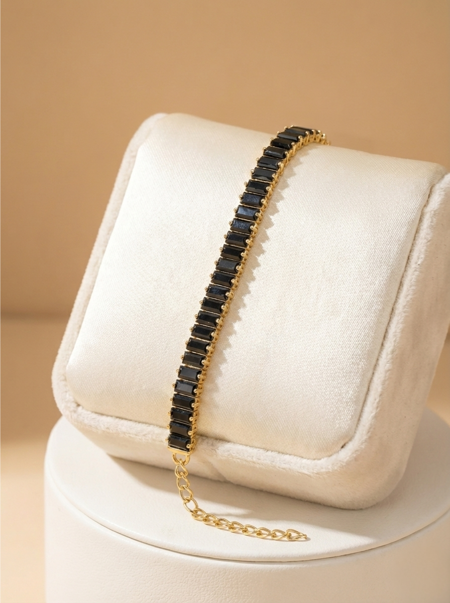 Necklace with black stones and gold chain on a white cushion against a beige background