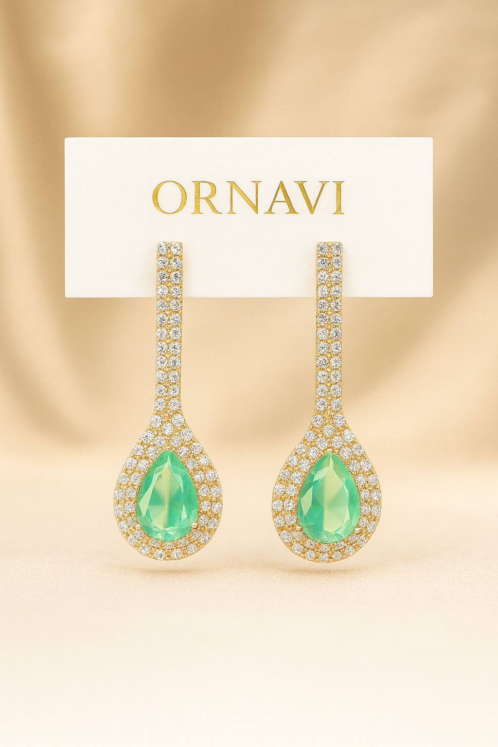 Ornate earrings with green gemstones on a beige background, featuring the brand 'ORNAVI'.