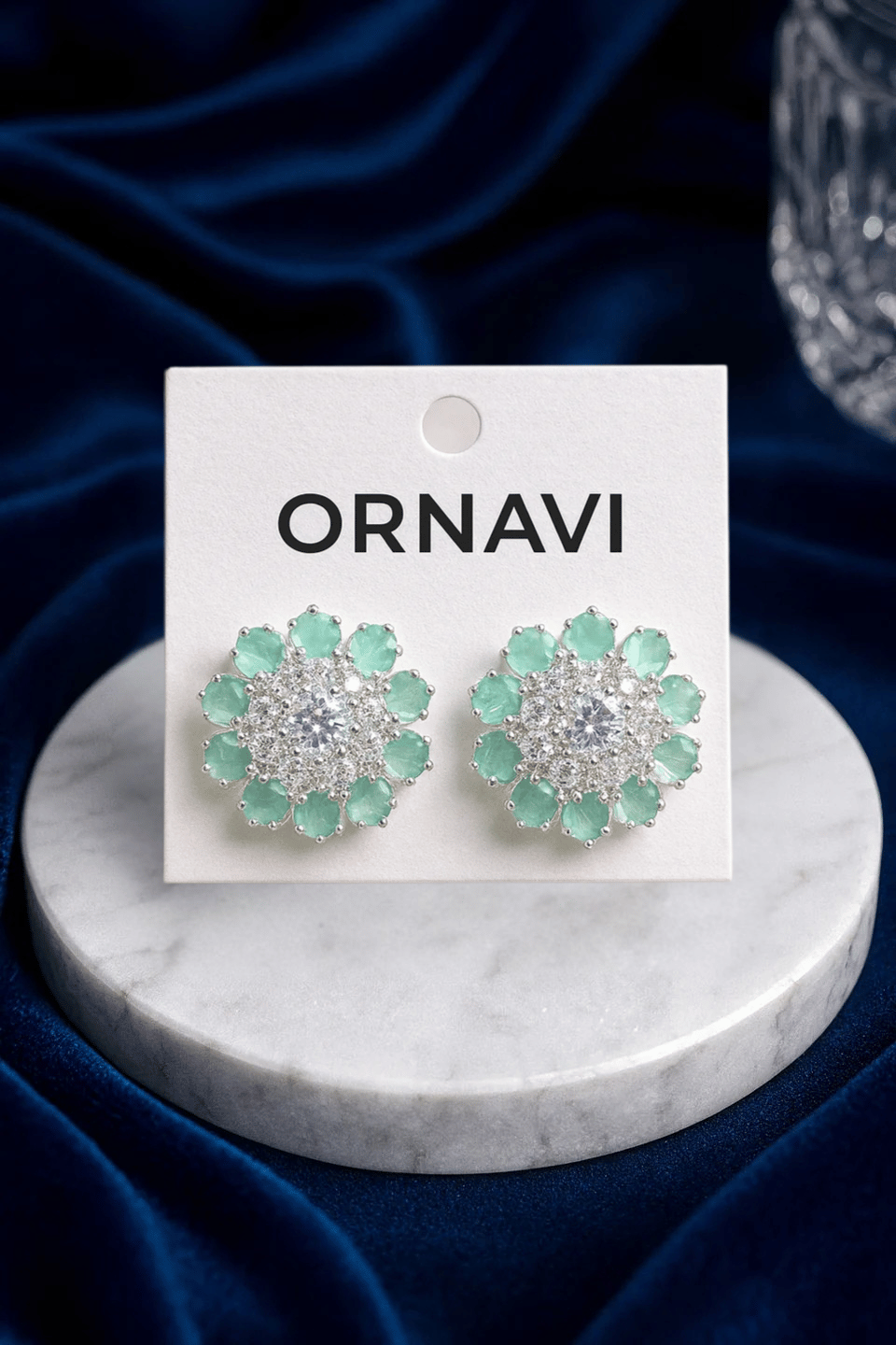 Ornavi earrings on a marble stand with a blue fabric background