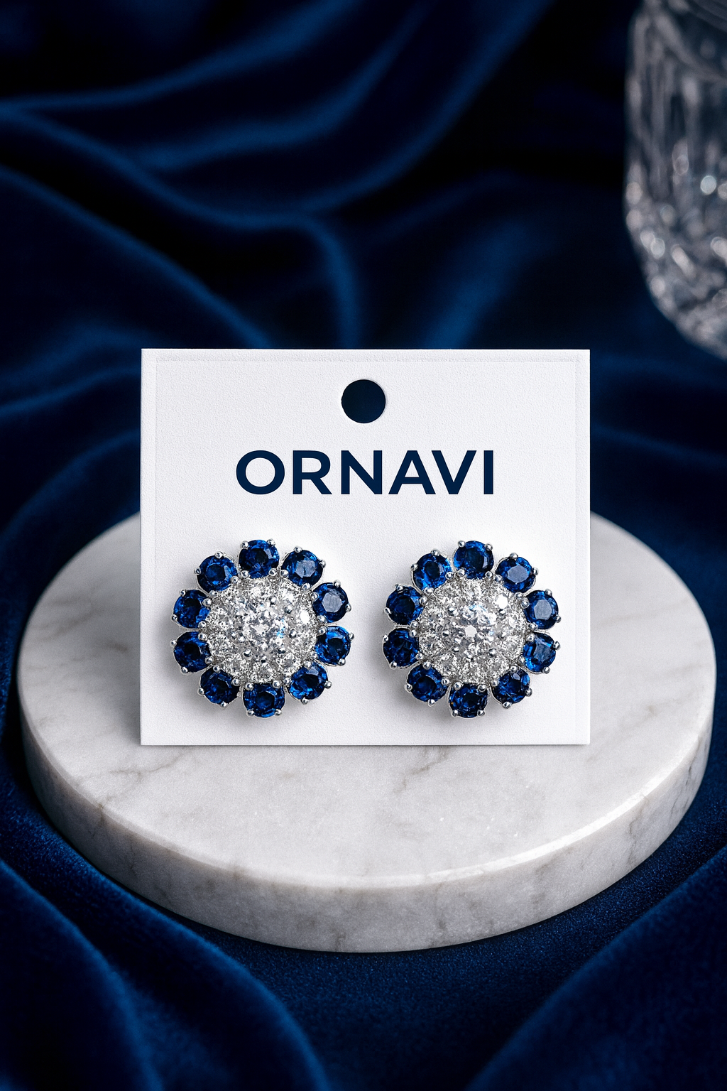 Ornavi earrings on a marble stand with a blue satin background