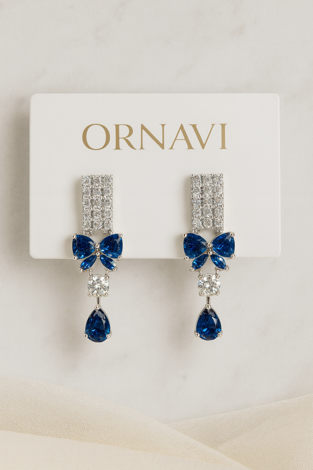 Pair of blue teardrop earrings with bow design on a white card with 'ORNAVI' branding.