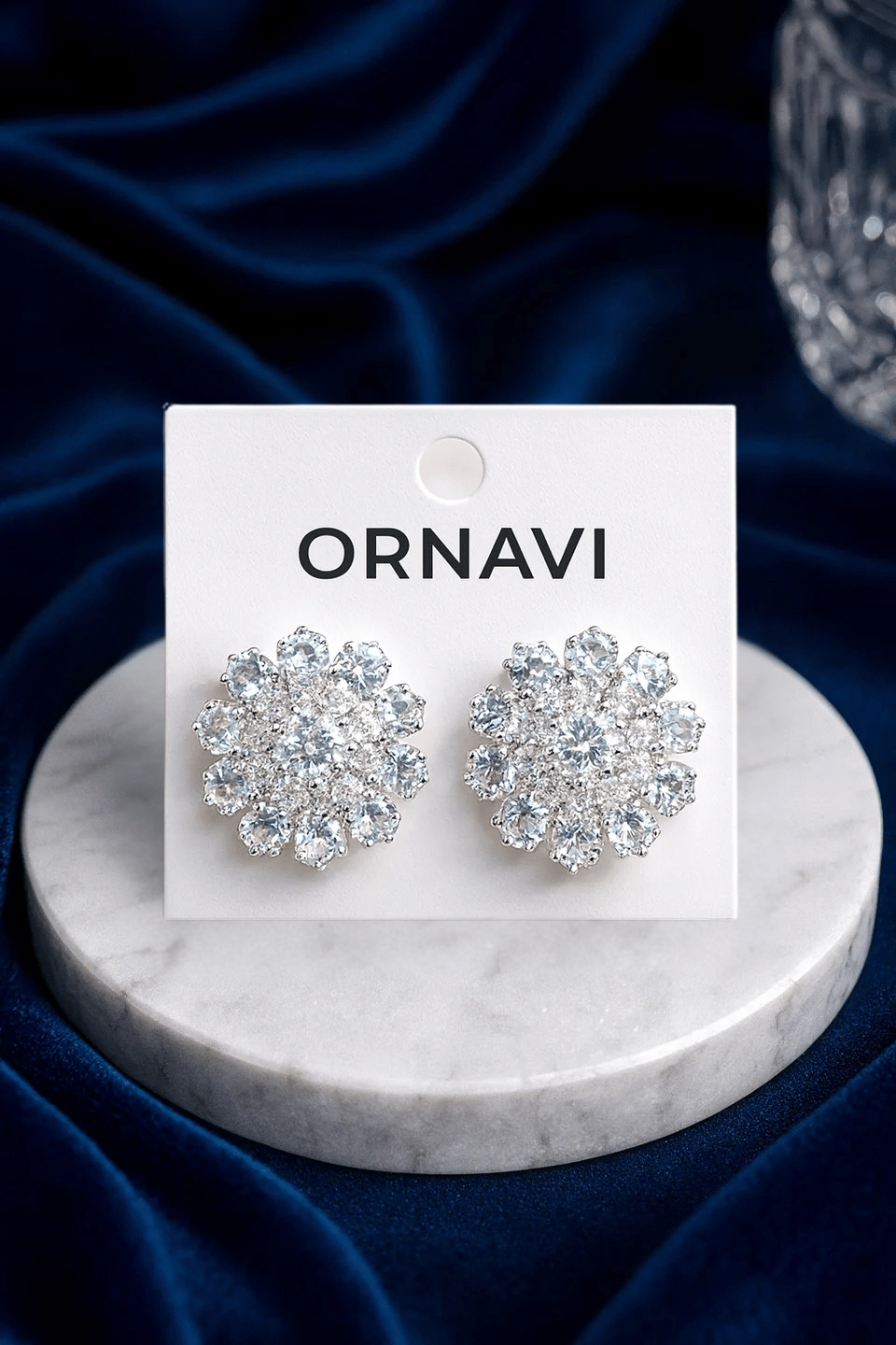 Silver earrings on an ORNAVI branded card with a blue fabric background