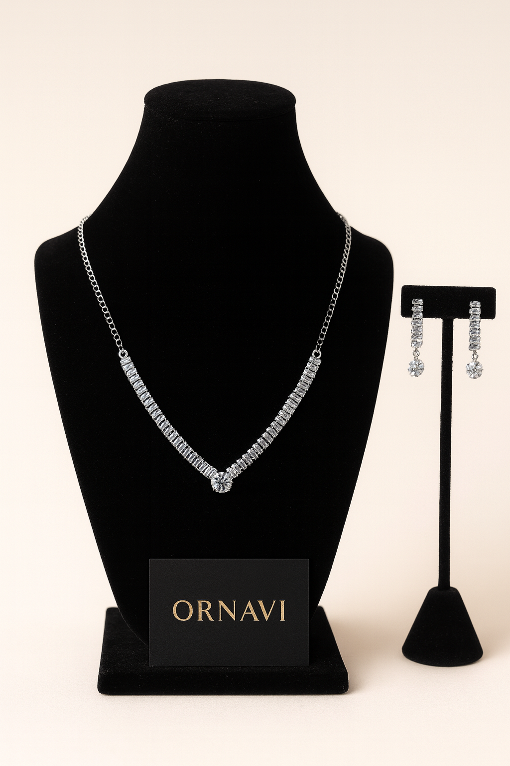 Silver necklace on a black bust and silver earrings on a stand with 'ORNAVI' branding.