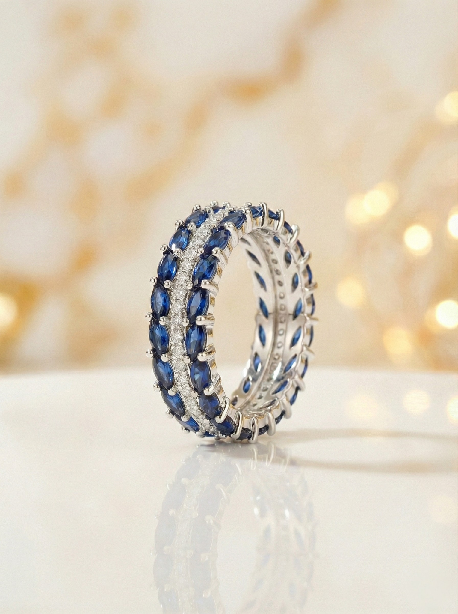 Silver ring with blue gemstones on a reflective surface with a blurred light background