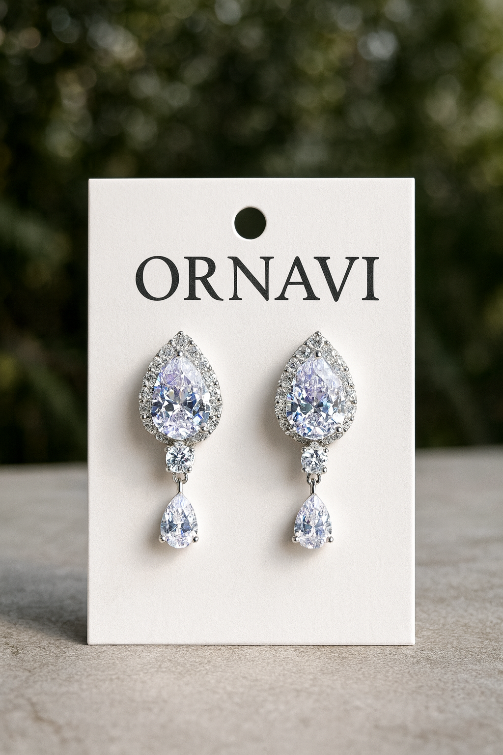 Teardrop-shaped earrings on a ORNAVI branded card with a blurred green background